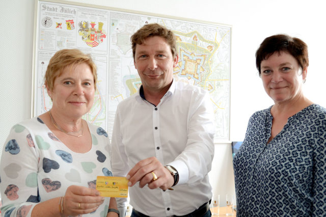 Bürgermeister Axel Fuchs (M) überreichte gemeinsam mit Anne Gatzen vom Amt für Stadtmarketing (r.) die 100. Ehrenamtskarte an Brigitte Barton-Wöllm (l.). Foto: Stadt Jülich/Stein