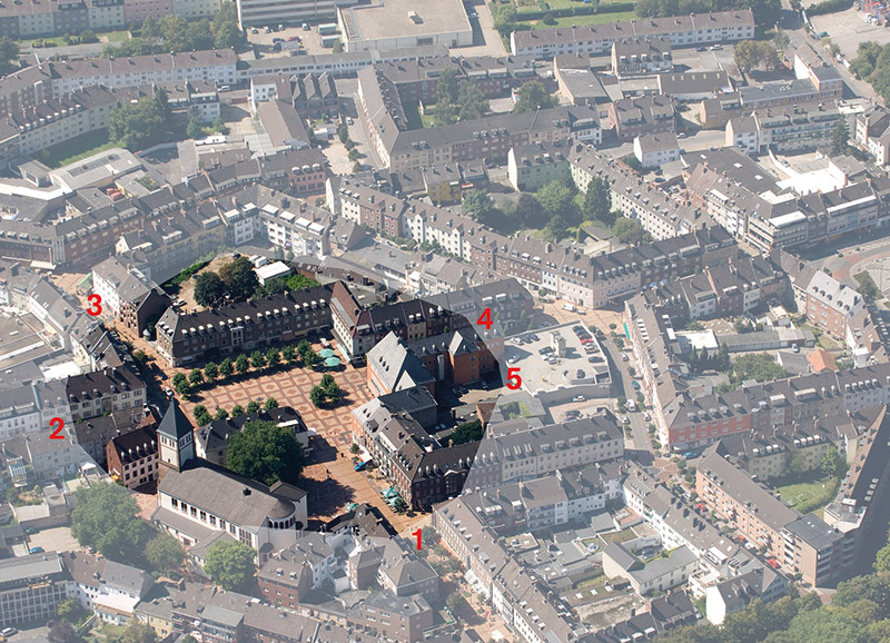 Auf allen vier Straßen zum Markt ist der Verlauf der Kastellmauer mit grauen Pflasterstreifen markiert (1-4), zu der die Fundstelle im Rathaushof gehört (5). Der massive Schutzring um das Zentrum war 1000 Jahre lang die Stadtmauer und später Grafenburg Jülichs (4.-14. Jh.). Die Kirche entstand aus einem Gebäude, das sich an diese massive Mauer schmiegte. Darum steht sie so schräg und zeigt nach Nordosten statt genau nach Osten wie andere Kirchen.